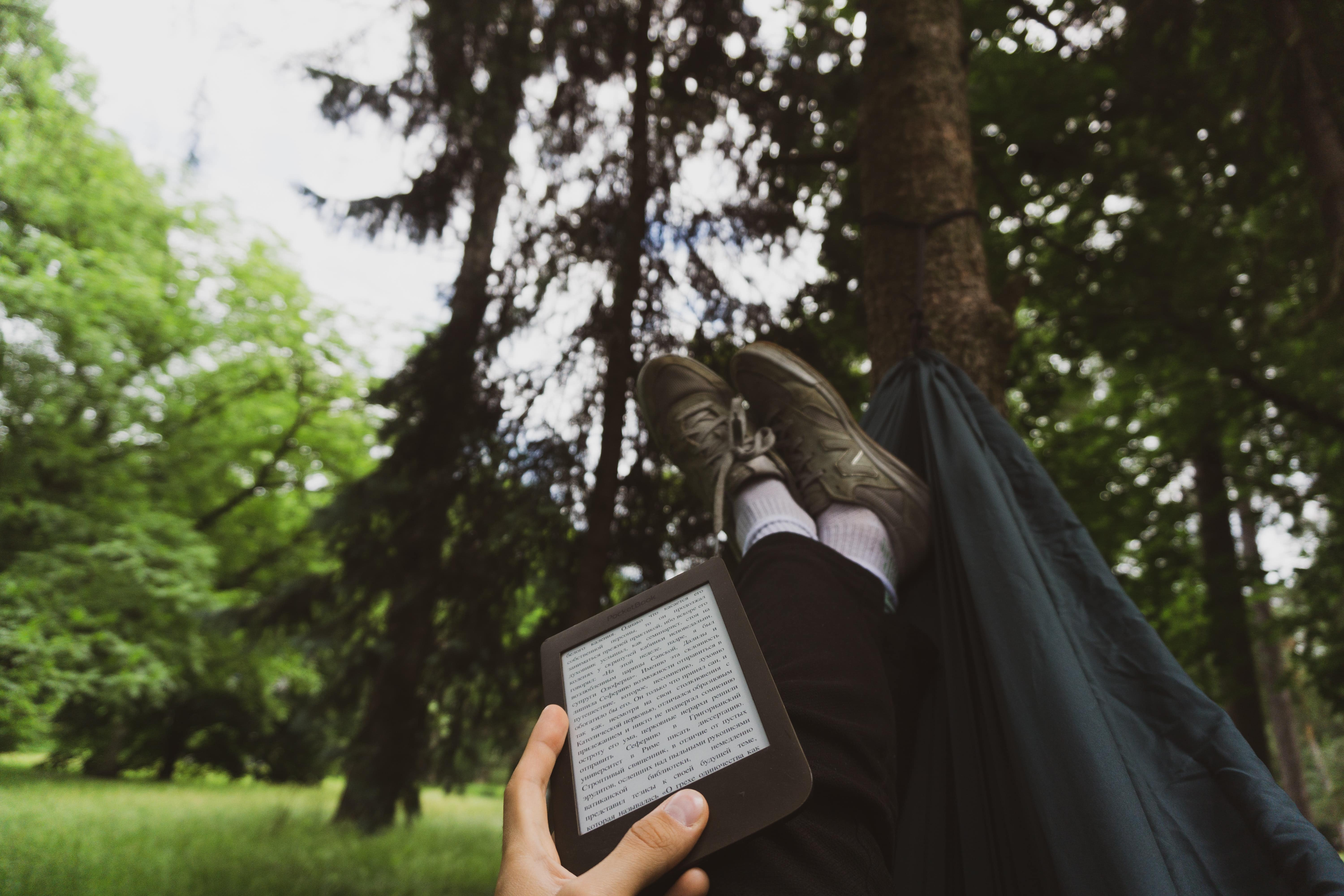 A person reading a Kindle lying in a hammock